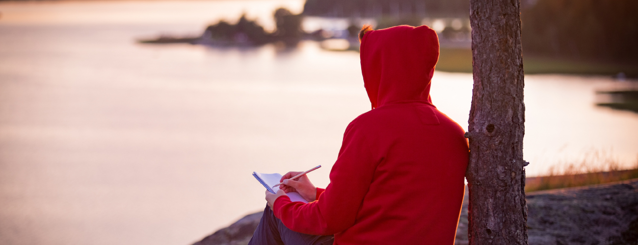 Keravan Suojakotiyhdistys ry / linkitsivun banneri - henkilö kirjoittaa kalliolla ja katselee järvelle