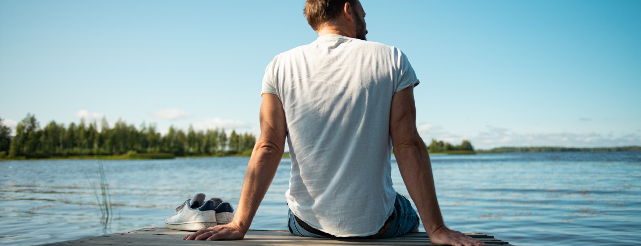 Mieshenkilö istuu laiturilla aurinkoisena kesäpäivänä